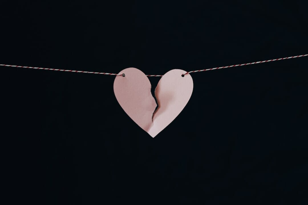 Breaking up with some you love. Pink broken heart held together by a tiny thin string.